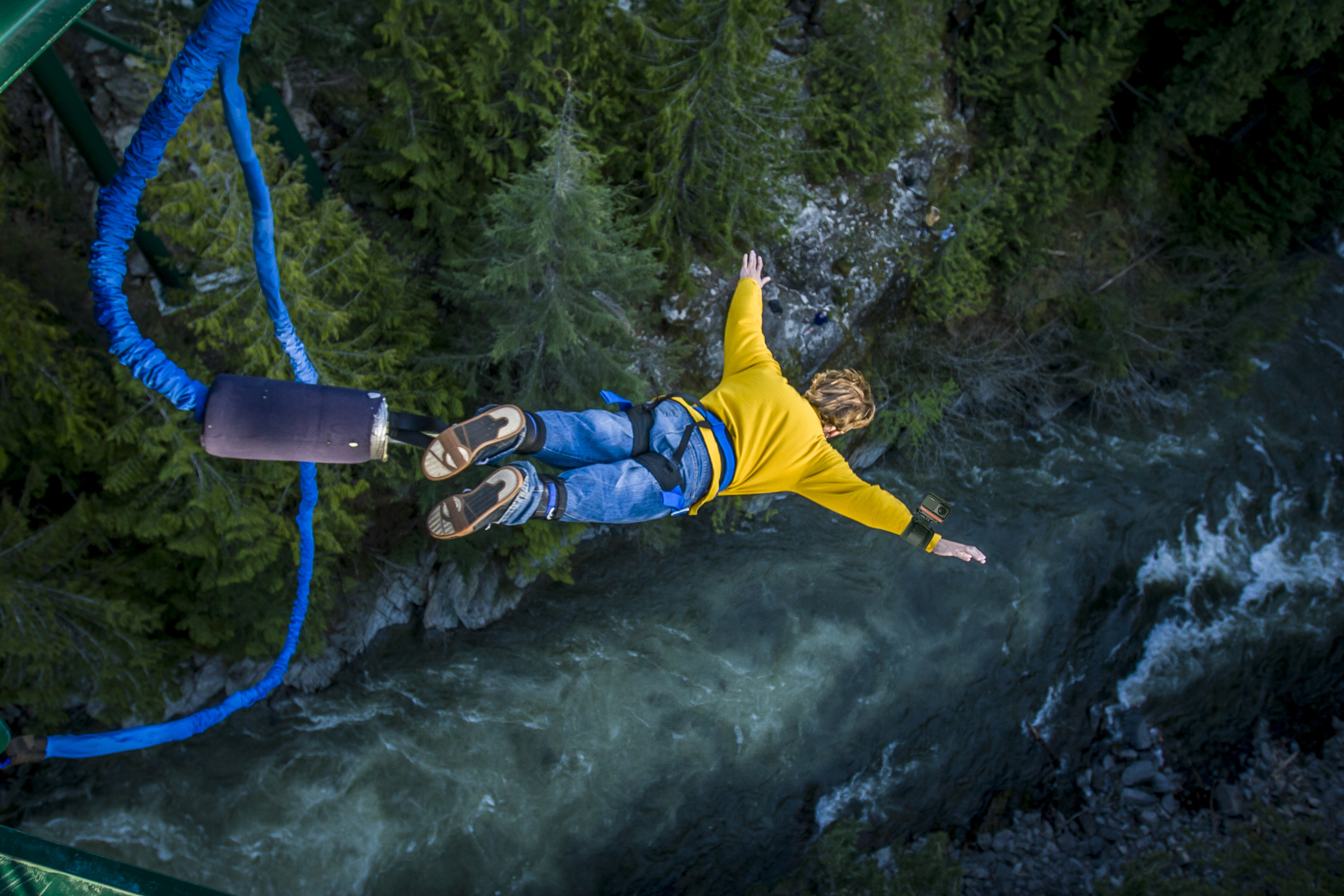 Eine Person in gelber Jacke springt von einer Brücke über einen Fluss.