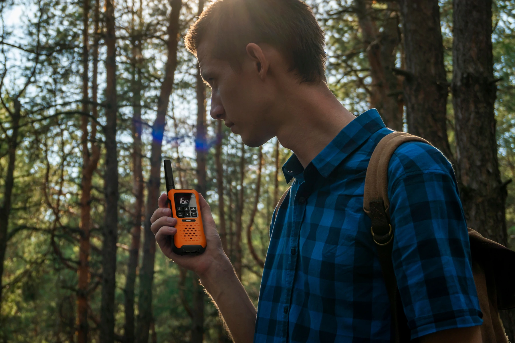 Ein Mann in blauem Hemd betrachtet ein oranges Walkie-Talkie in einer Waldumgebung.
