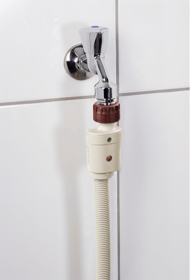 Un rubinetto collegato a un tubo e un filtro dell'acqua su una parete piastrellata bianca.