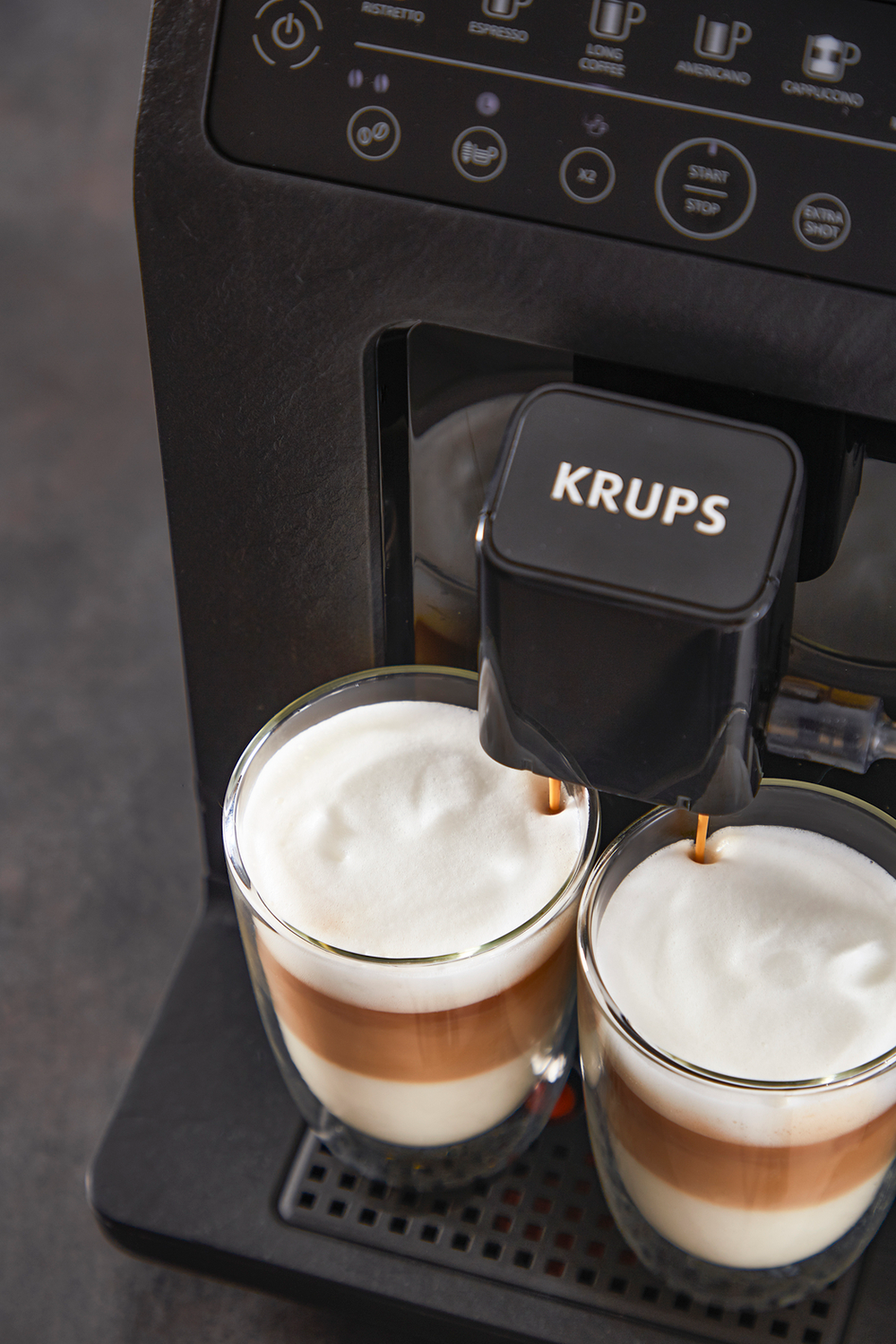 Een koffiemachine die koffie en melkschuim in twee glazen schenkt.