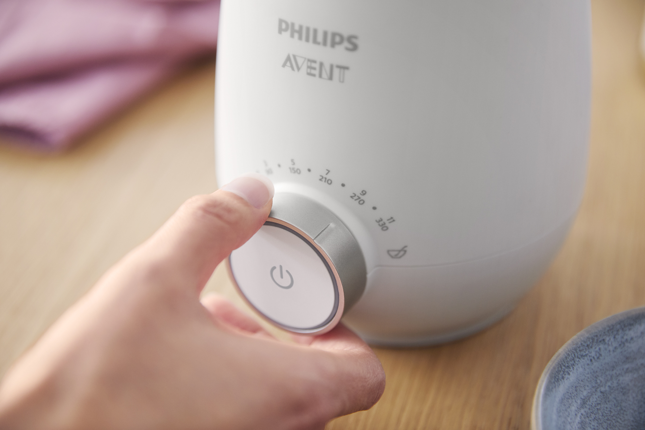 Hand die een witte Philips Avent flessenwarmer afstelt. Grijze draaiknop met cijfers en het aan/uit-symbool.