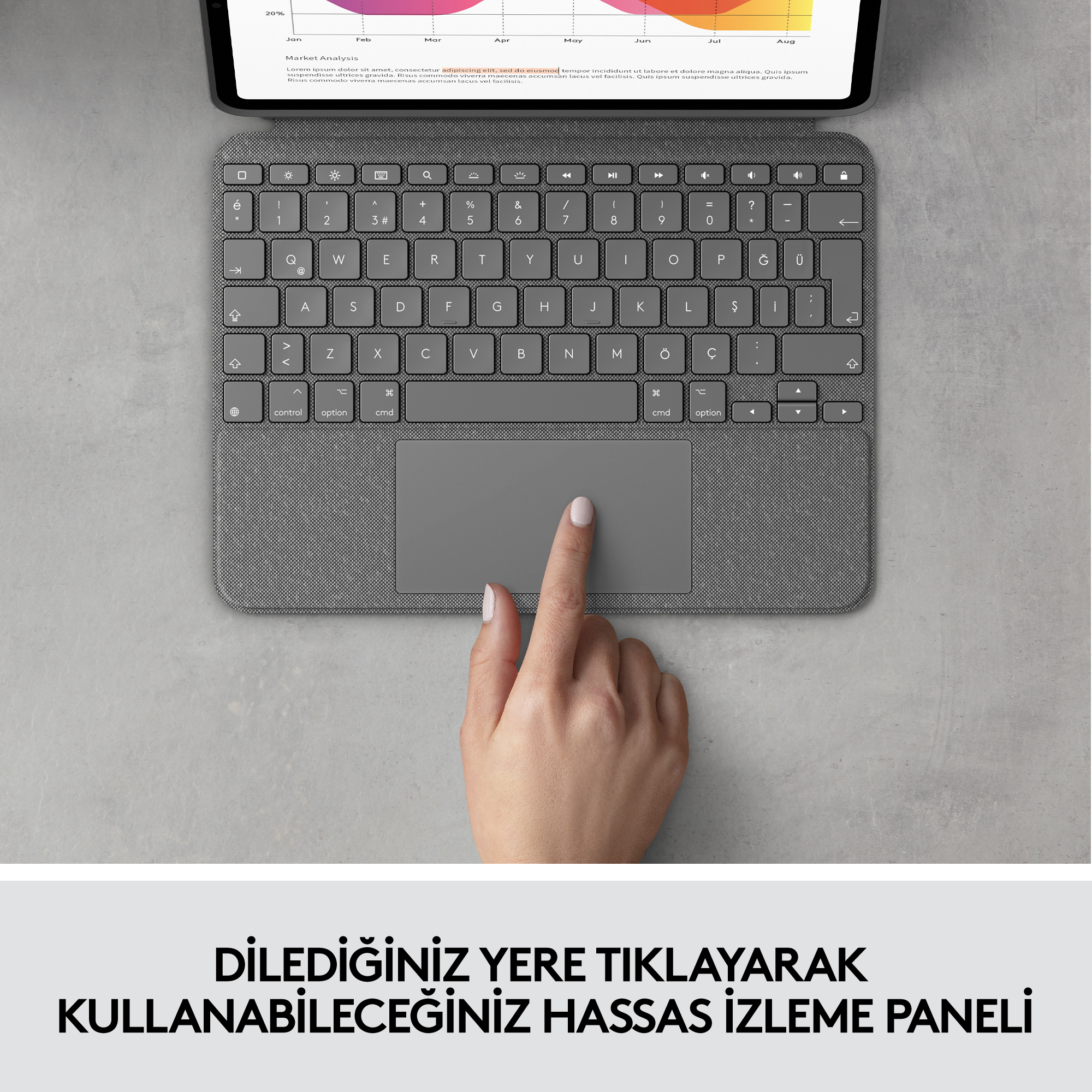 Bir dokunmatik yüzeye sahip gri bir klavyeye dokunan el. Klavye, arka planda bir tablet bulunan bir masada.