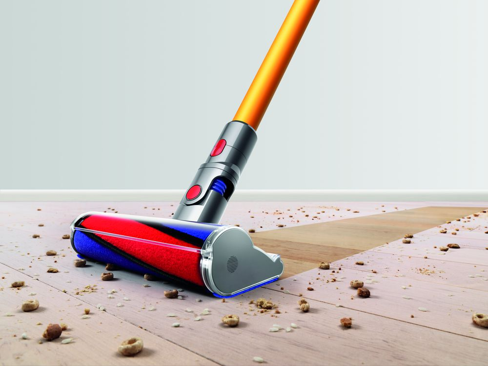 Un cabezal de aspiradora limpiando un suelo de madera. El cabezal es naranja y plateado, con suciedad y residuos visibles.