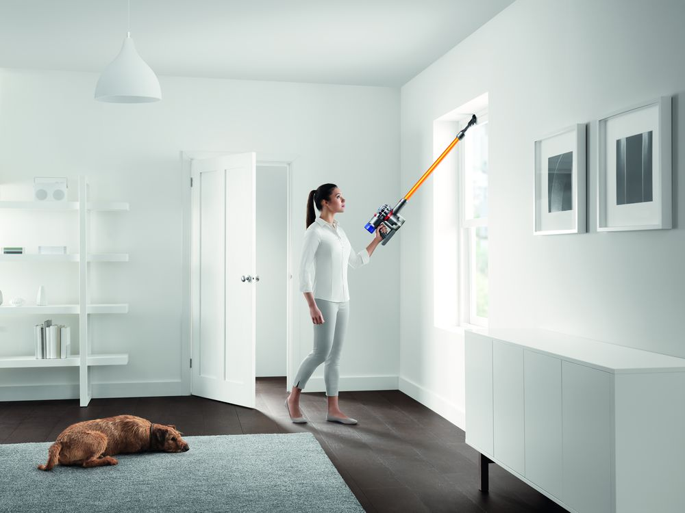 Mujer aspirando una ventana; perro en el suelo, paredes blancas, decoración moderna.