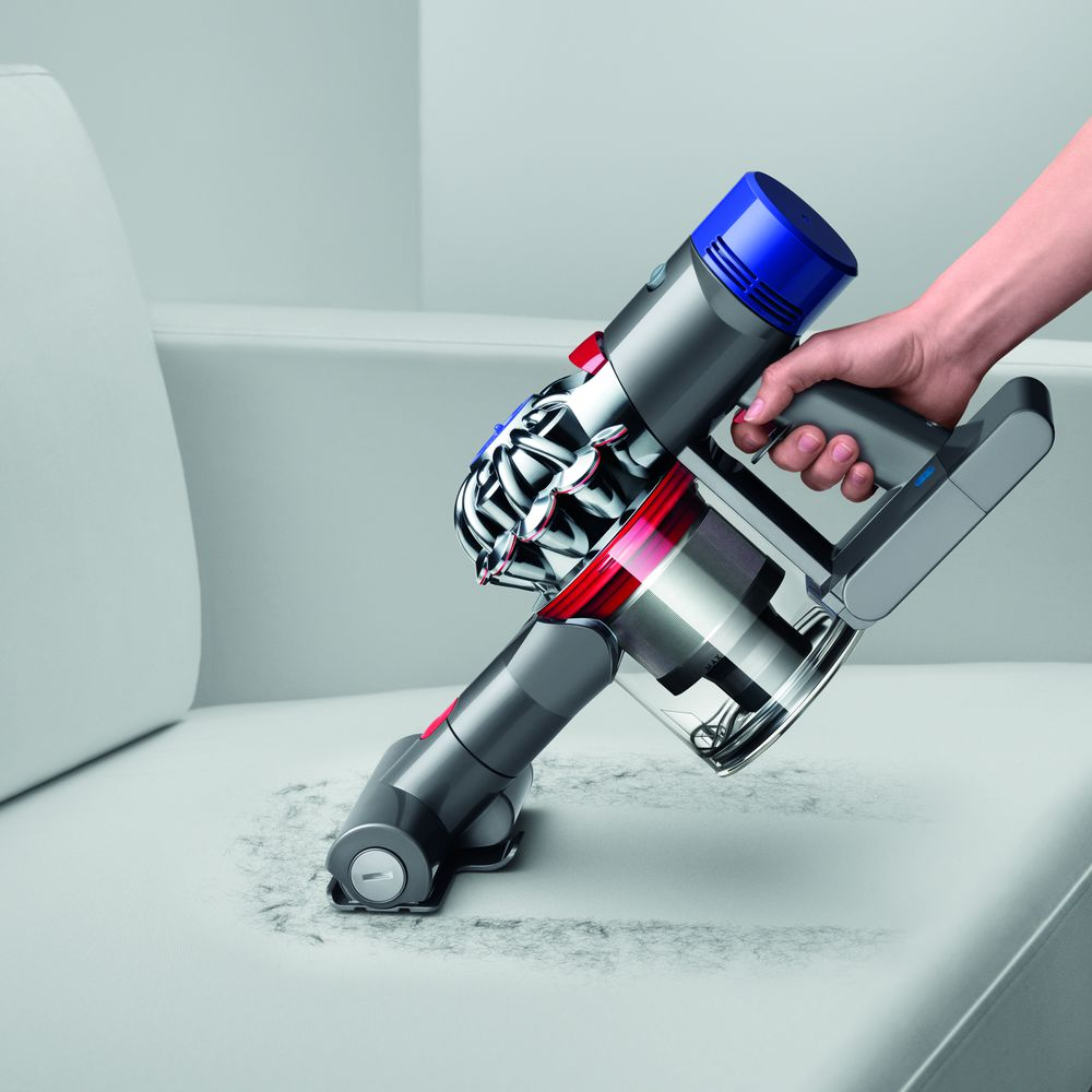 Una persona aspira un sofá gris con una aspiradora de mano Dyson.