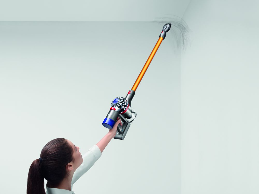 Una mujer usando una aspiradora en una pared blanca. La aspiradora es naranja y azul.