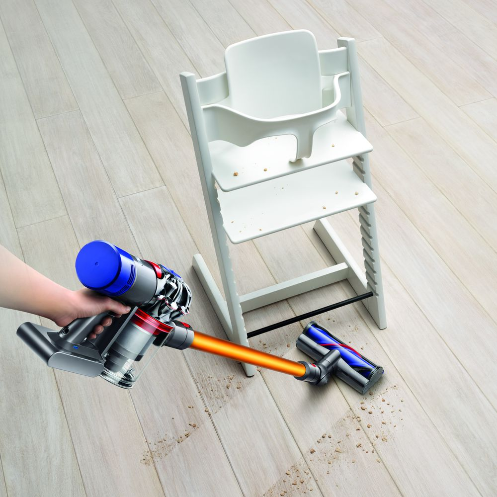 Una persona aspira un suelo de madera con una aspiradora Dyson, cerca de una trona.