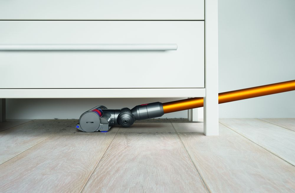 Cabezal de aspiradora debajo de un gabinete blanco, limpiando un piso de madera.