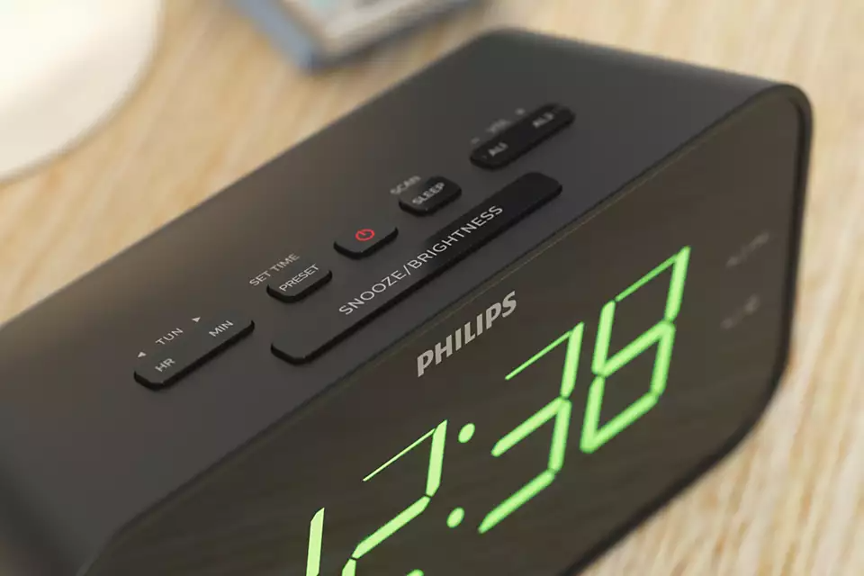 Réveil Philips noir avec affichage numérique vert indiquant l'heure. Les boutons sont visibles en haut.