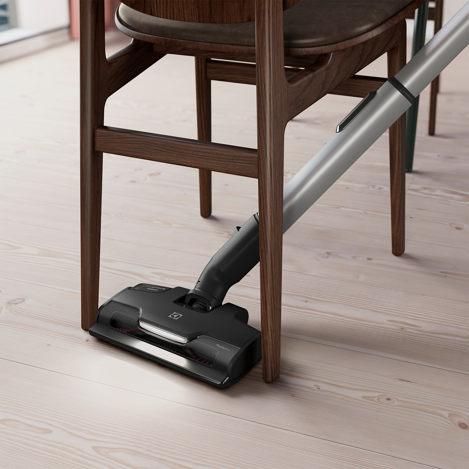 Una testina per aspirapolvere che pulisce sotto una sedia. Il pavimento è in legno. La sedia ha gambe di legno.