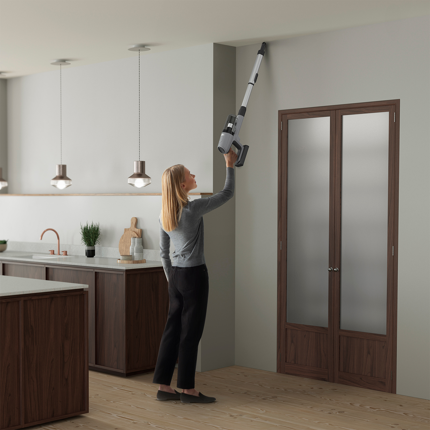 Donna che aspira il soffitto con un aspirapolvere senza fili in cucina.
