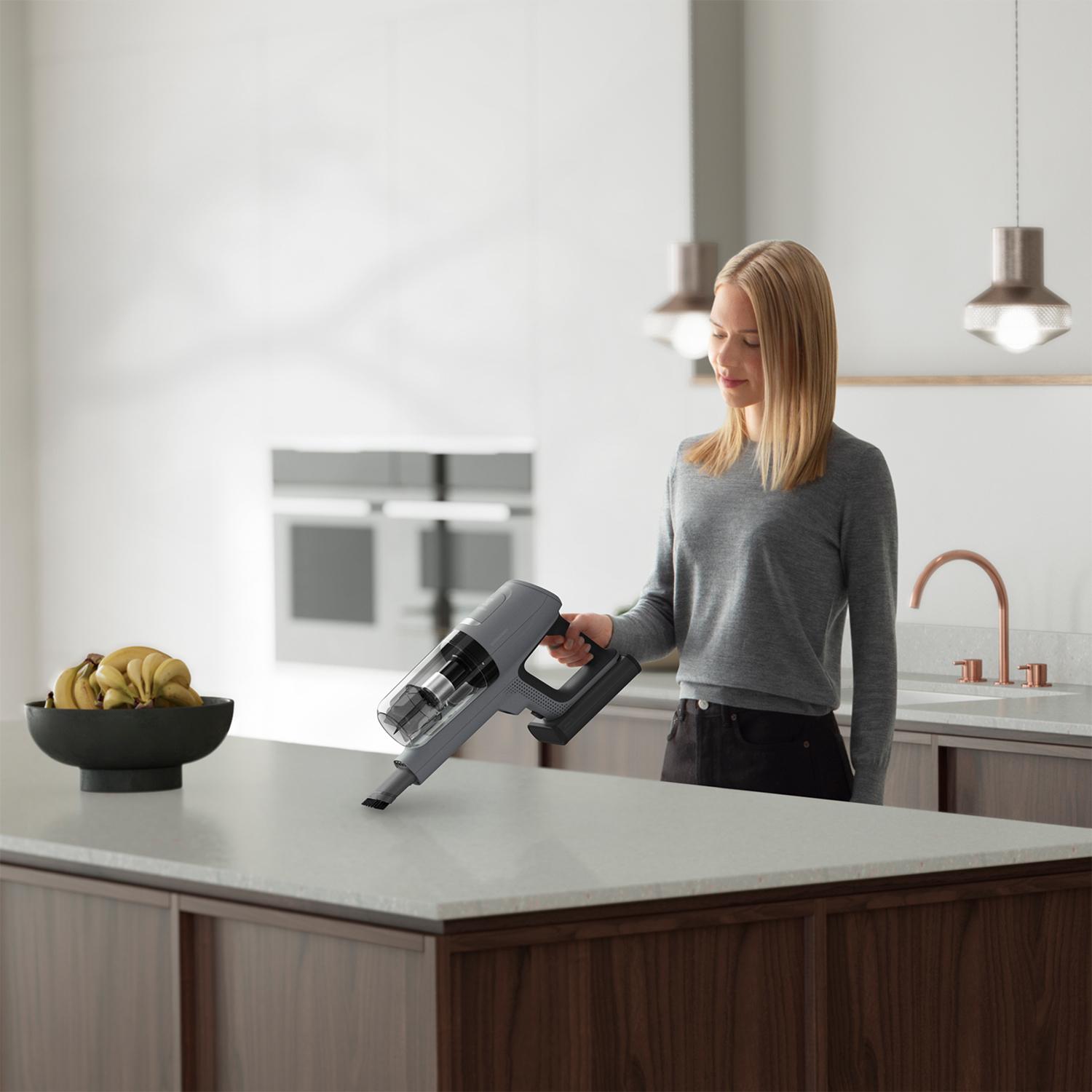 Una donna che usa un aspirapolvere portatile su un piano di lavoro bianco in cucina.
