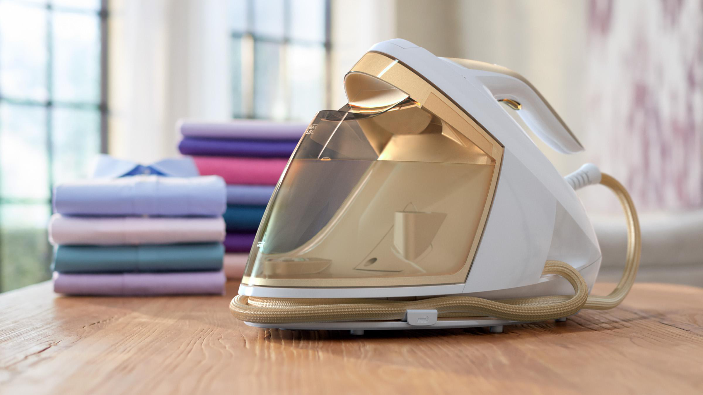 Ein weißes und goldenes Bügeleisen mit Wassertank und ein Stapel gefalteter Hemden auf einem Holztisch.