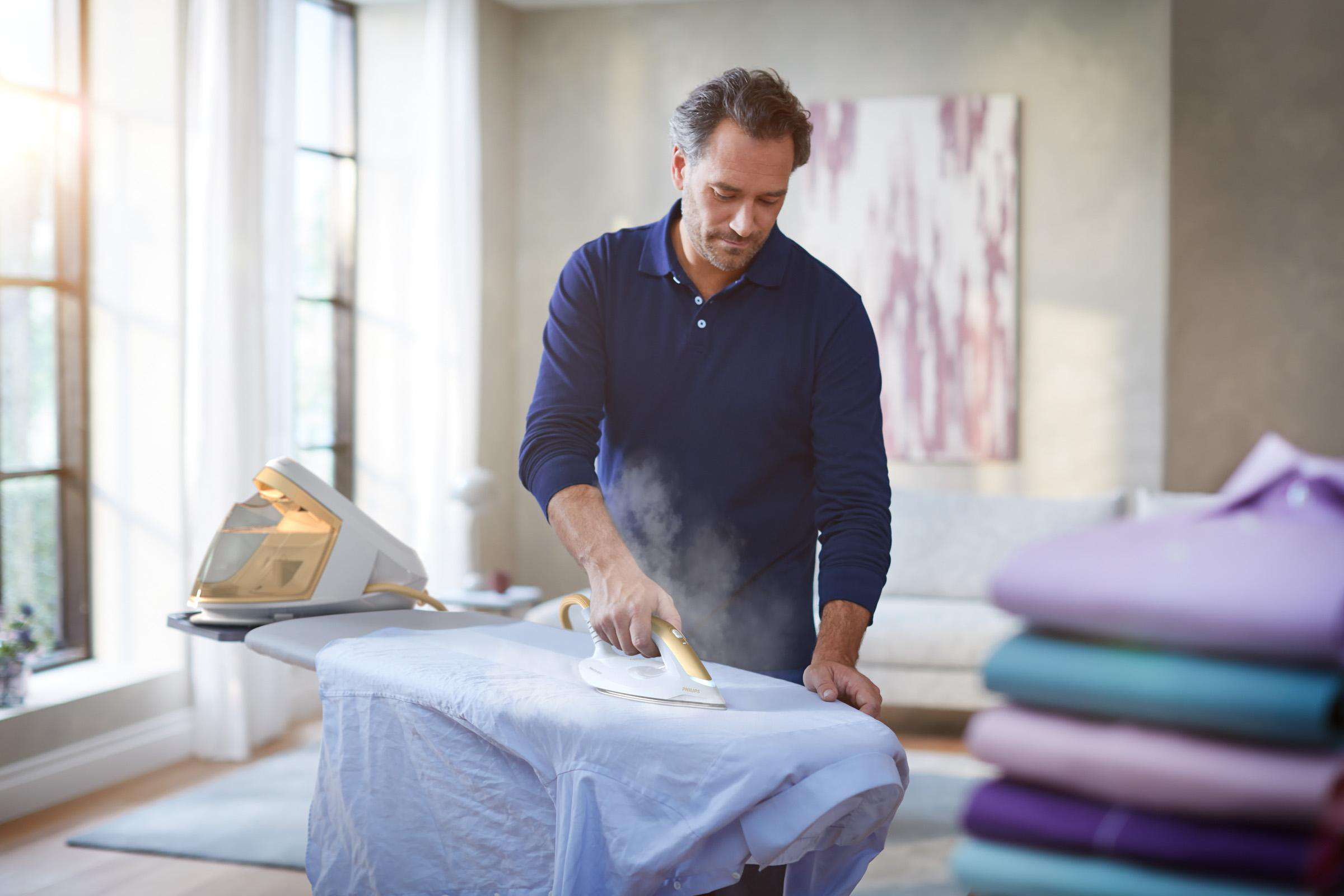 Mann bügelt ein weißes Hemd auf einem Bügelbrett, Dampf sichtbar.