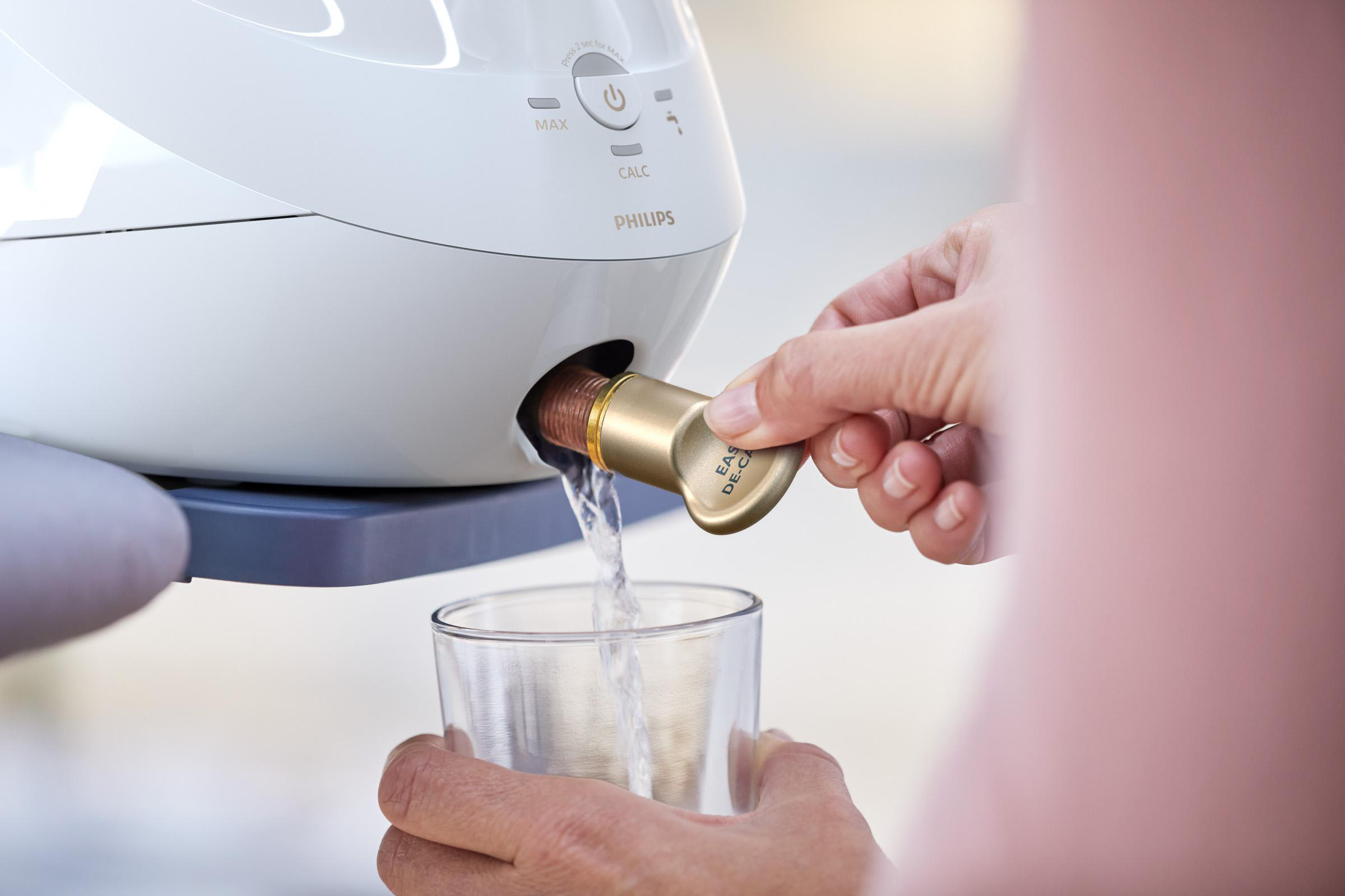 Person füllt ein Glas mit Wasser aus einem Philips-Gerät, unter Verwendung eines goldfarbenen Ausgusses.