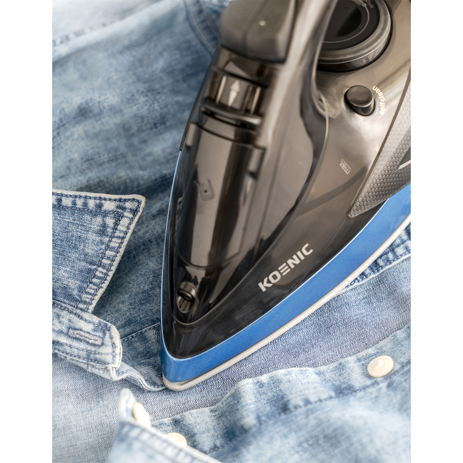 Un ferro da stiro sta stirando una camicia di jeans. Il ferro è nero e blu, con il marchio KOENIC.
