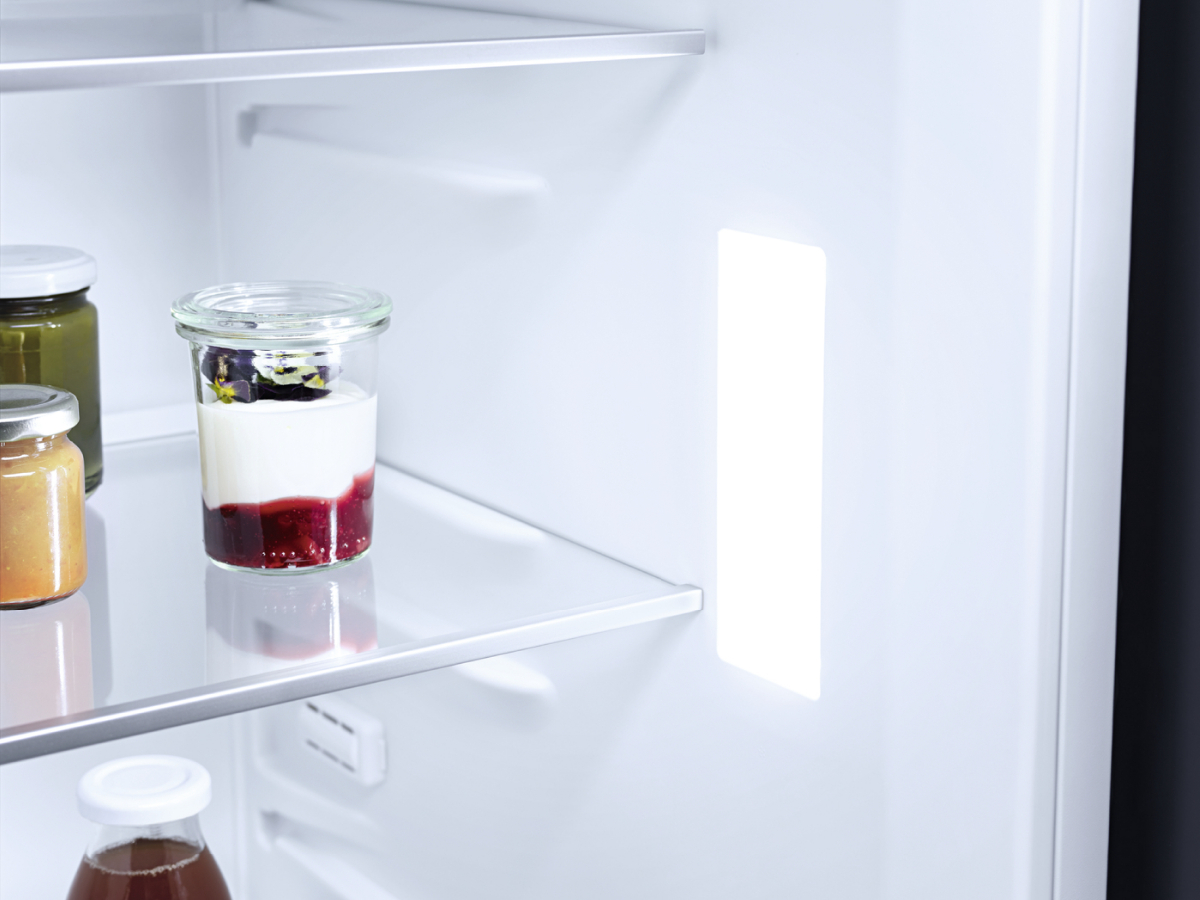Im Kühlschrank, Gläser mit Essen auf einem Glasregal. Licht scheint von der Seite.
