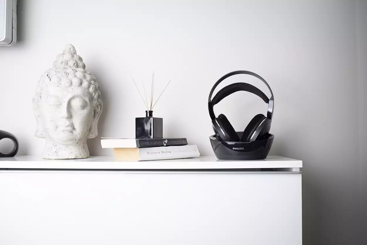 Table blanche avec tête de Bouddha, livres, diffuseur et casque dans base noire.