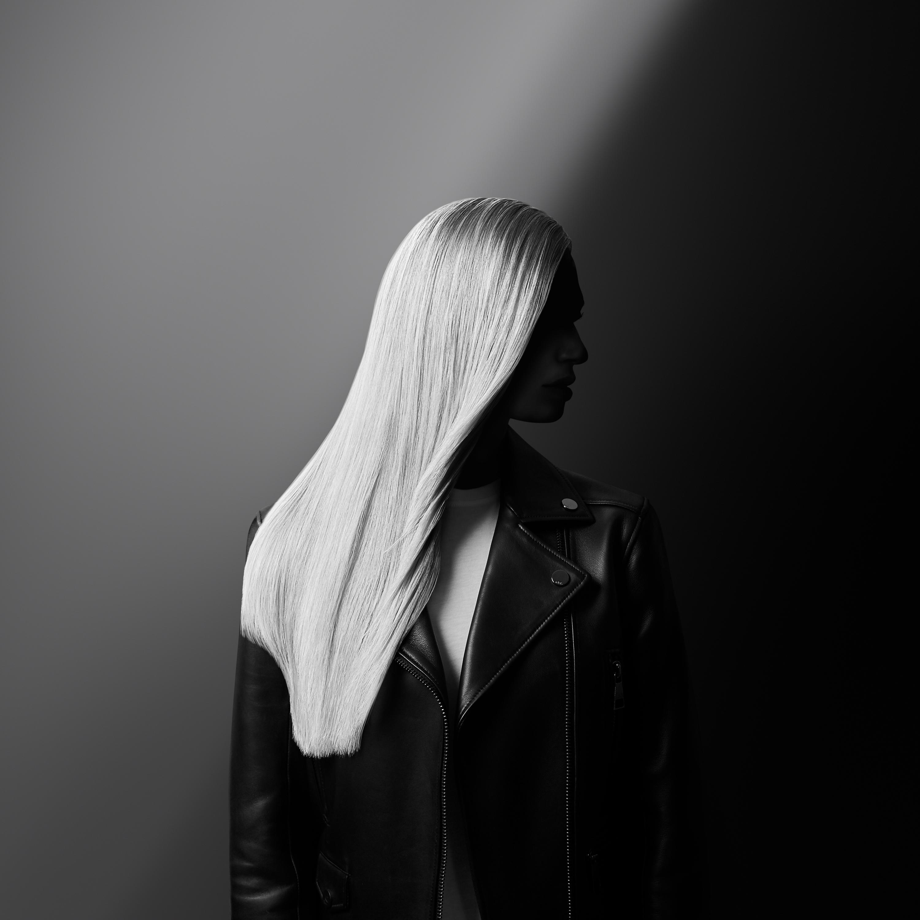Eine Person mit langen, glatten, weißen Haaren und einer schwarzen Lederjacke, im Schatten.
