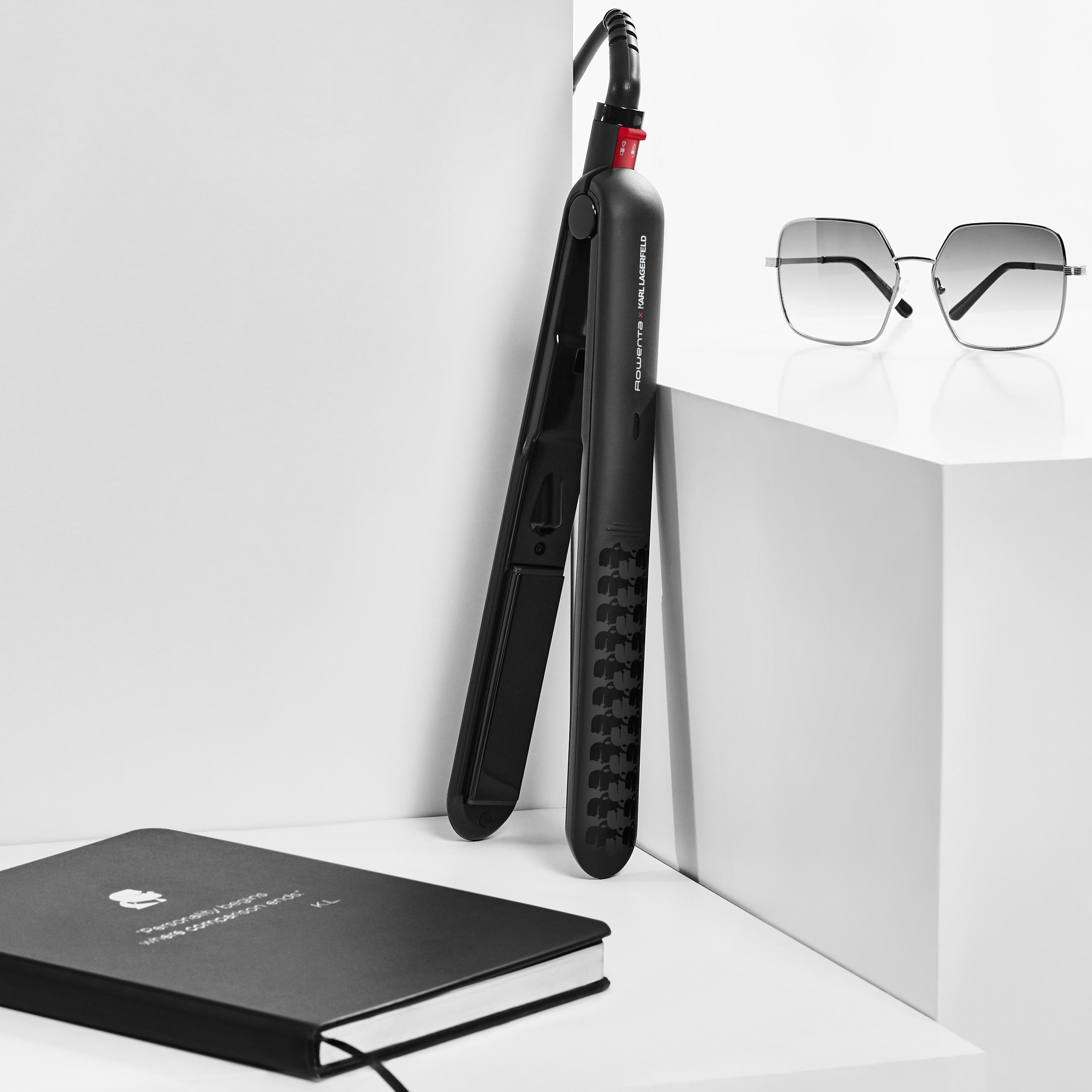 Ein Glätteisen und eine Sonnenbrille auf einer weißen Oberfläche neben einem Notizbuch.