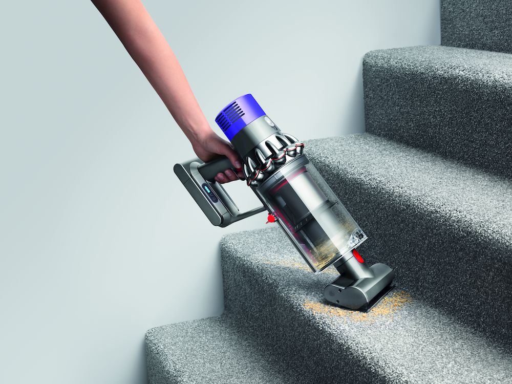 Una persona aspirando escaleras alfombradas grises con una aspiradora Dyson inalámbrica.