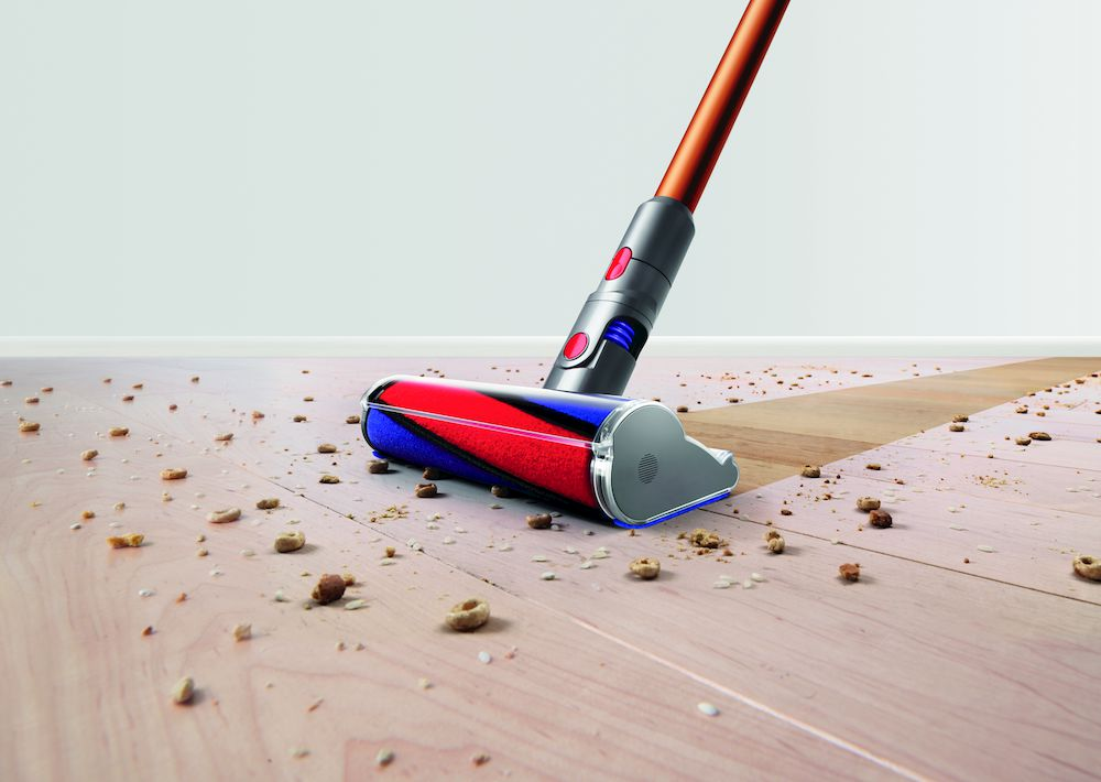 Un cabezal de aspiradora con un rodillo rojo y azul está limpiando un piso de madera con escombros.