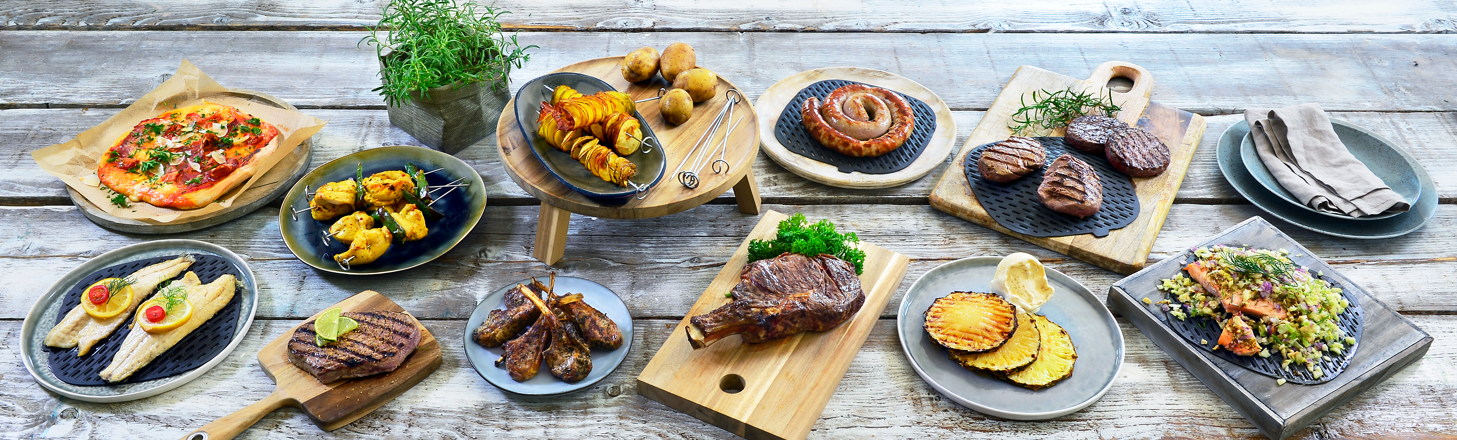 Variety of prepared food dishes on a wooden table, including pizza, meat, and vegetables.