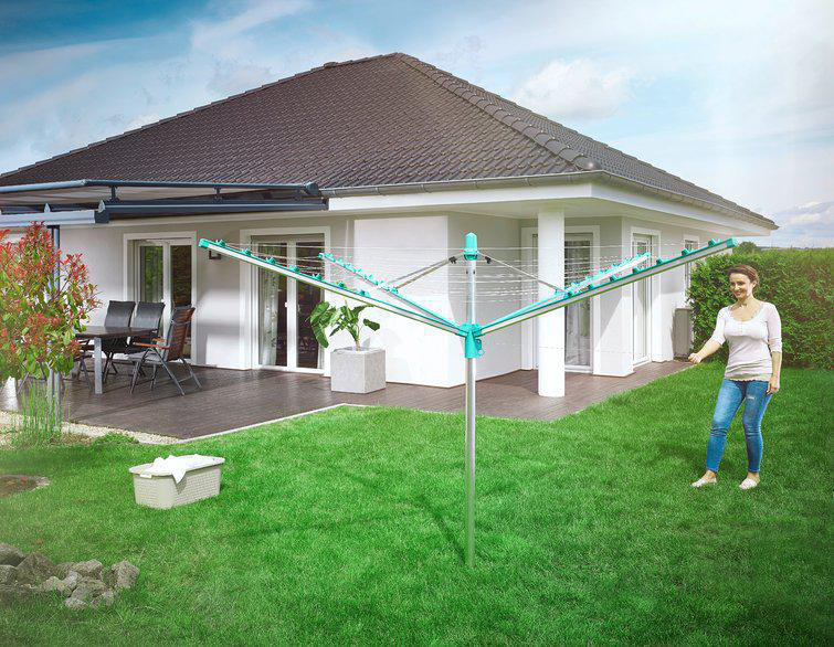 Frau in der Nähe eines Hauses mit einem Wäschetrockner in einem grünen Garten. Das Haus hat ein dunkles Dach.