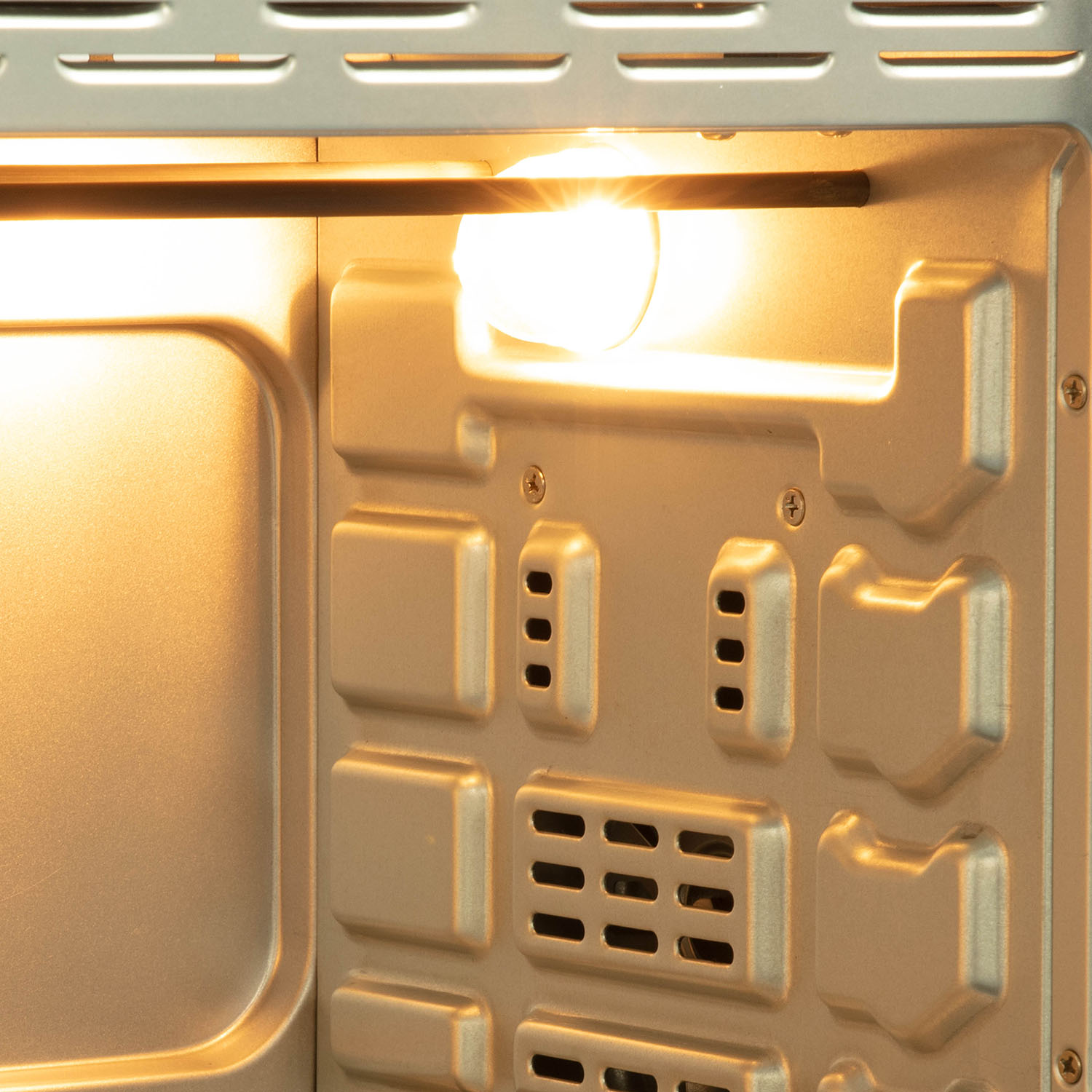 Inside of an oven with a light on. Silver interior with vents, and a bright light at the top.
