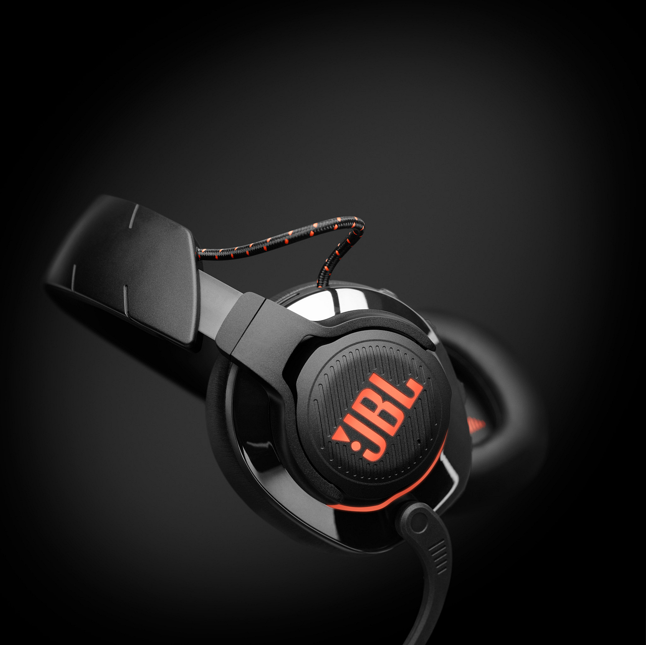 Schwarzes JBL-Gaming-Headset mit orangefarbenen Akzenten, leicht angewinkelt. Schwarzer Hintergrund.