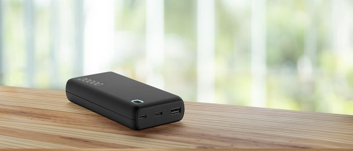 Schwarze Powerbank auf Holztisch. Hintergrund zeigt verschwommenes Fenster.