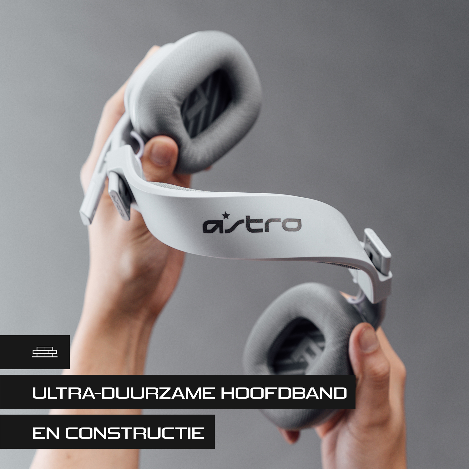 Een witte gamingheadset die door handen wordt vastgehouden. De headset heeft grijze oorschelpen en het woord 'astro'.
