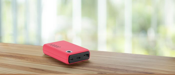 Eine rote Powerbank auf einem Holztisch. Der Hintergrund zeigt eine verschwommene Ansicht einer grünen, unscharfen Umgebung.