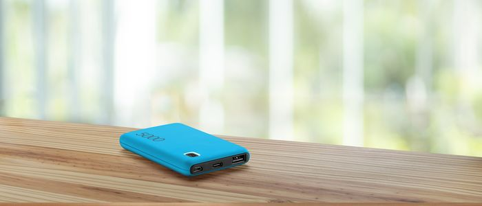 Blaue Powerbank auf einem Holztisch, mit verschwommenem grün-weißem Hintergrund.