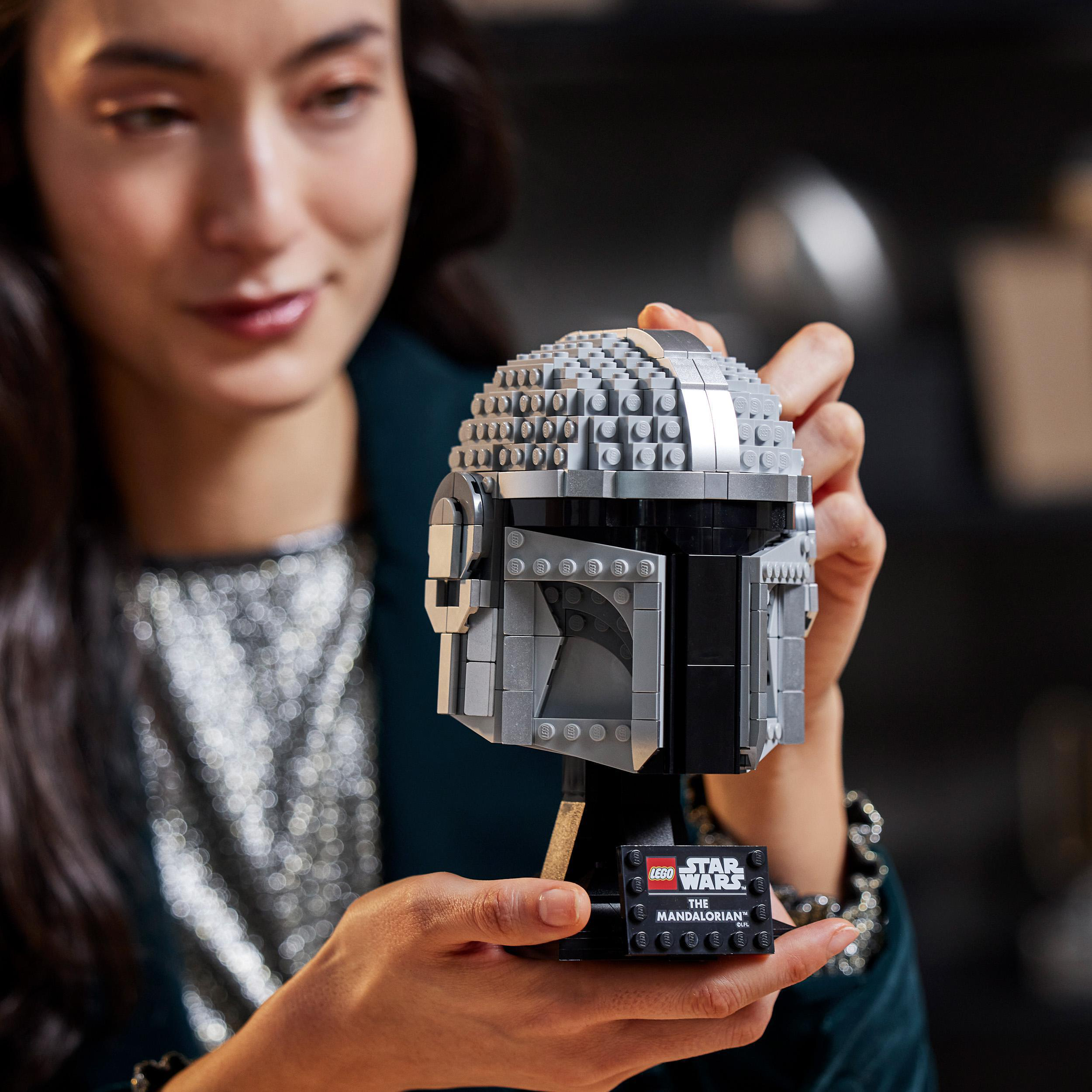 Eine Frau hält einen Lego Star Wars Mandalorianer Helm. Der Helm ist grau und detailliert.