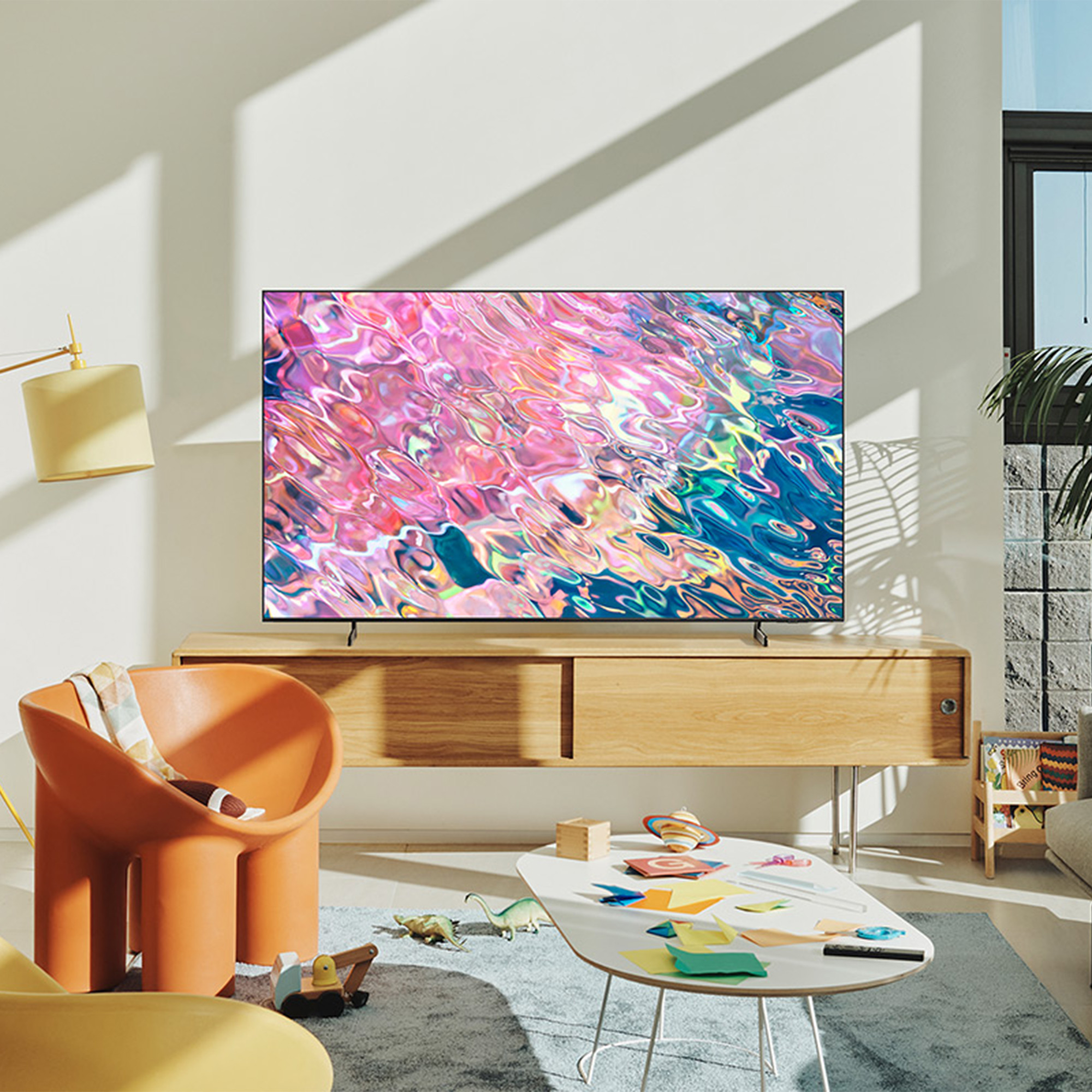 Sala de estar con un televisor grande en un mueble de madera, una pintura colorida y una silla naranja.