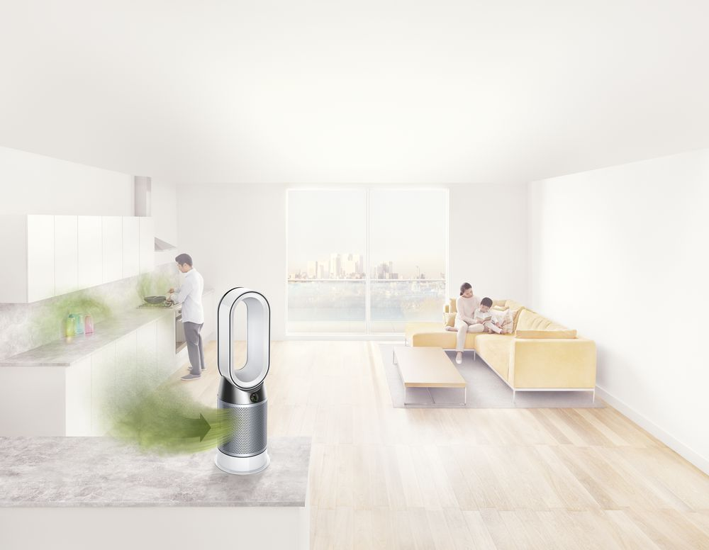 Un purificador de aire Dyson en una habitación con una cocina y personas sentadas en un sofá.
