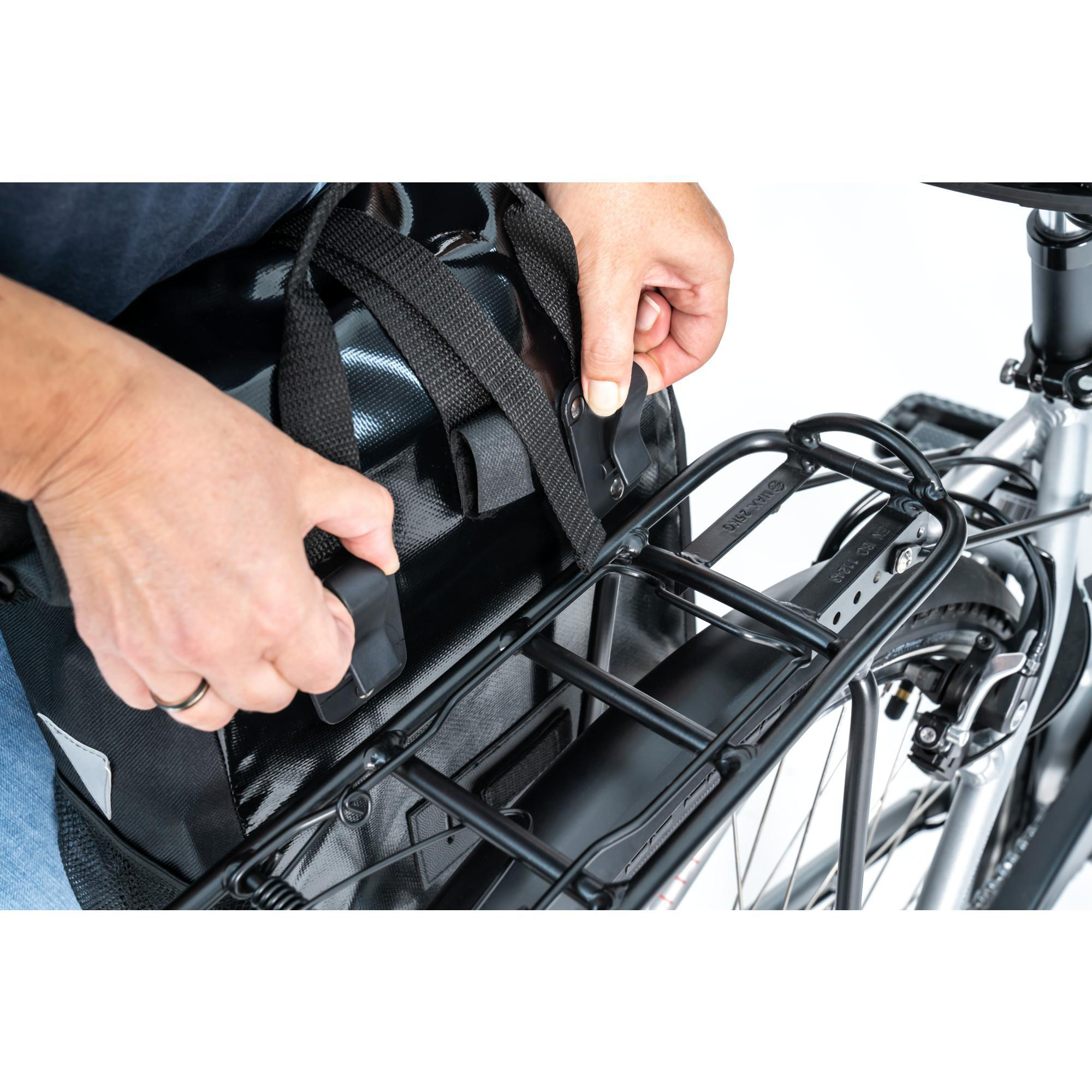 Hände einer Person befestigen eine schwarze Tasche an einem Fahrradgepäckträger, Nahaufnahme.