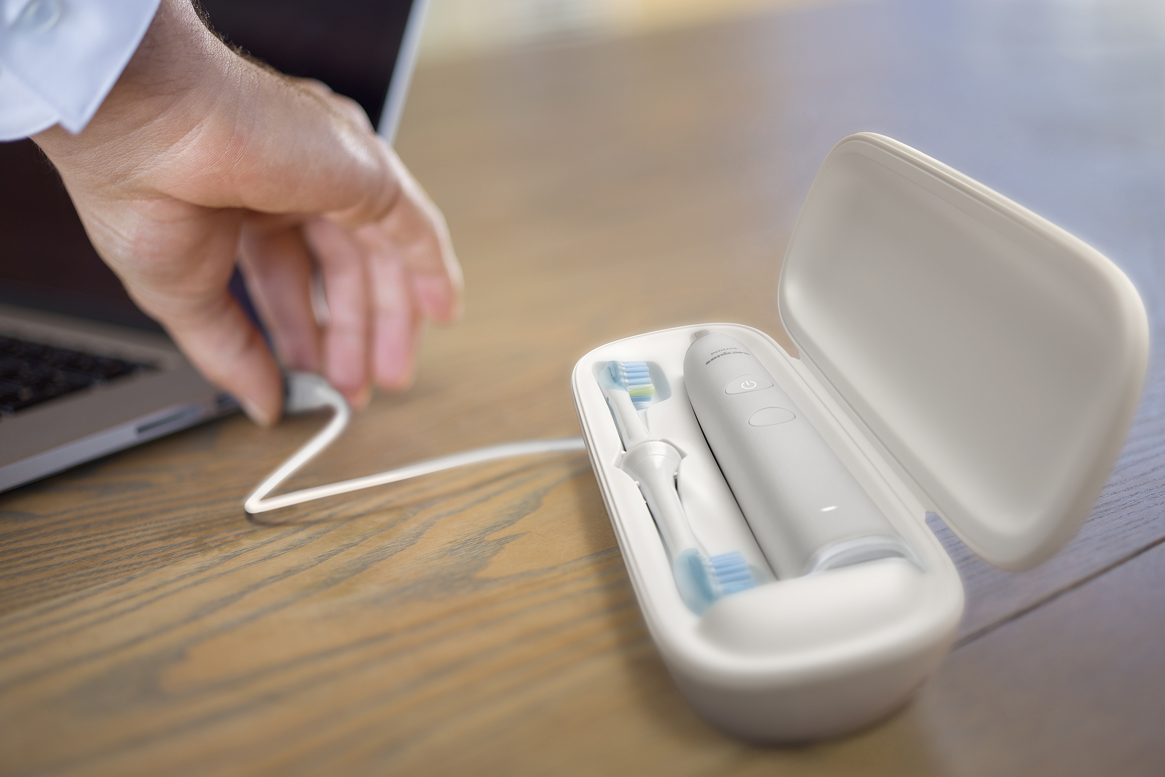Une main branche un câble USB blanc sur un ordinateur portable. Un étui blanc pour brosse à dents est ouvert à côté.