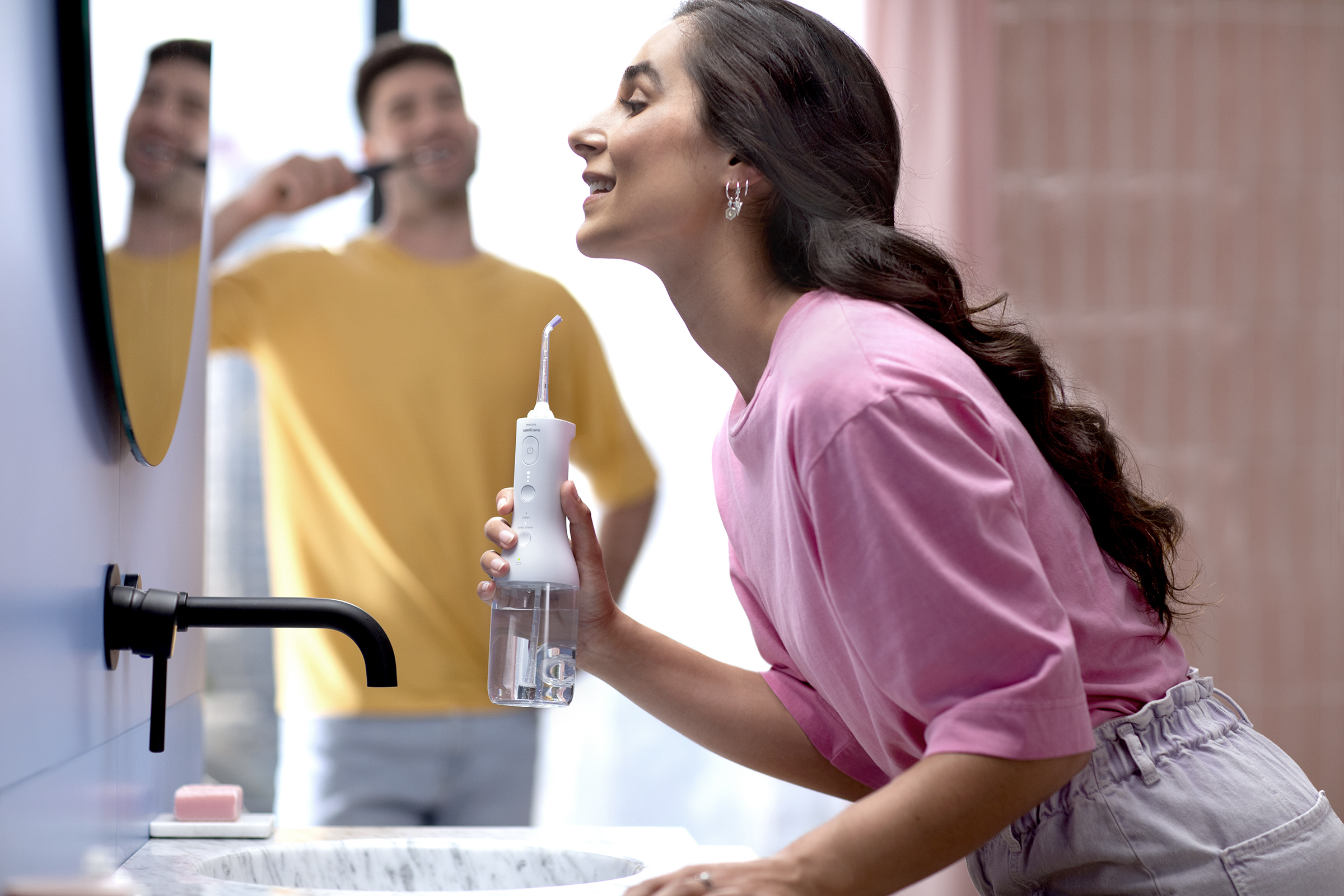 Femme utilisant un hydropulseur dans la salle de bain, homme se brossant les dents dans le miroir.