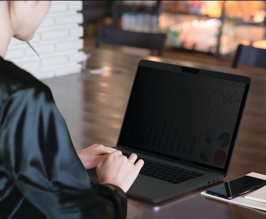 Személy laptopon dolgozik az asztalnál. A képernyő sötét, grafikonokat mutat.