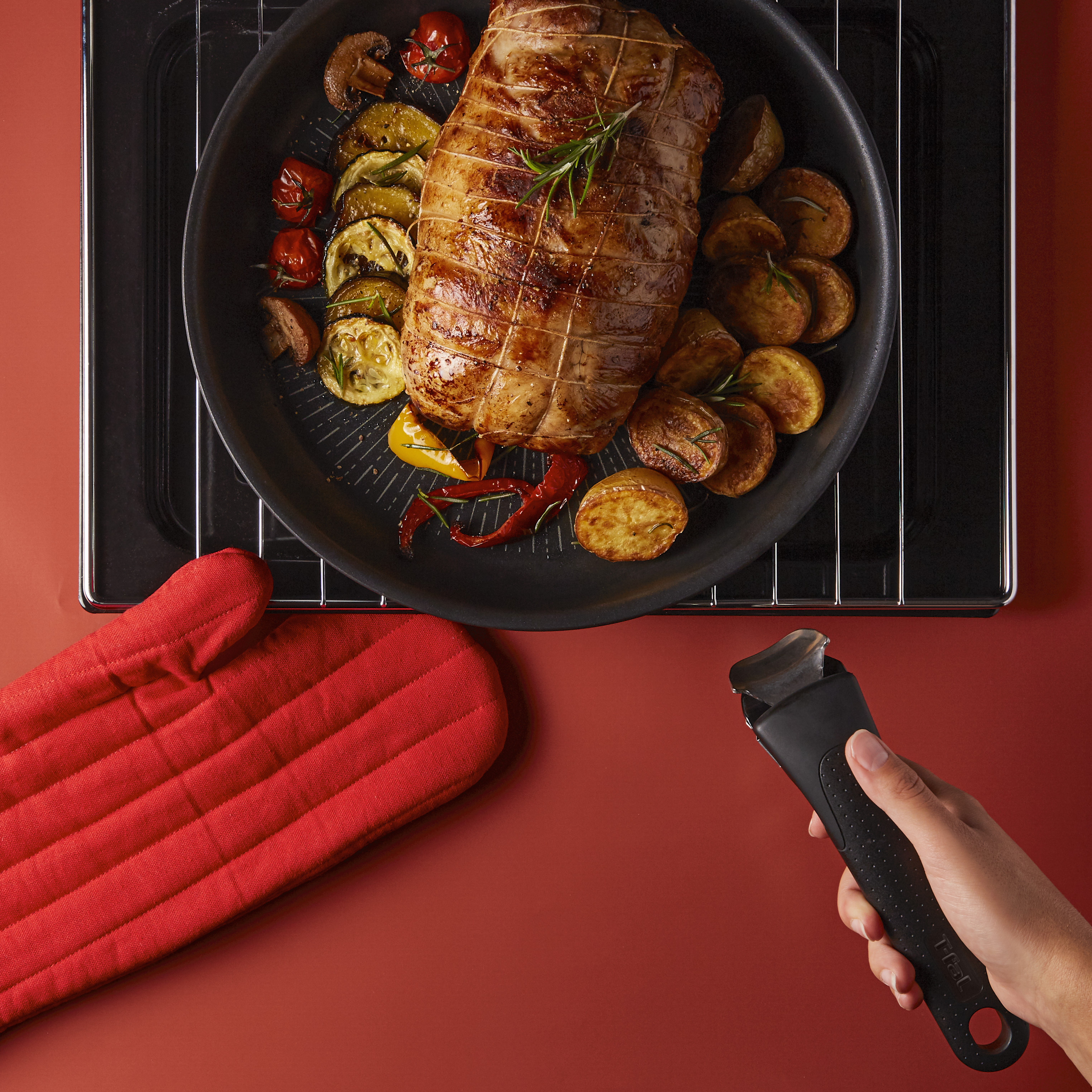 Viande rôtie avec des légumes dans une poêle. Un gant de four rouge et une poignée sont sur la table.