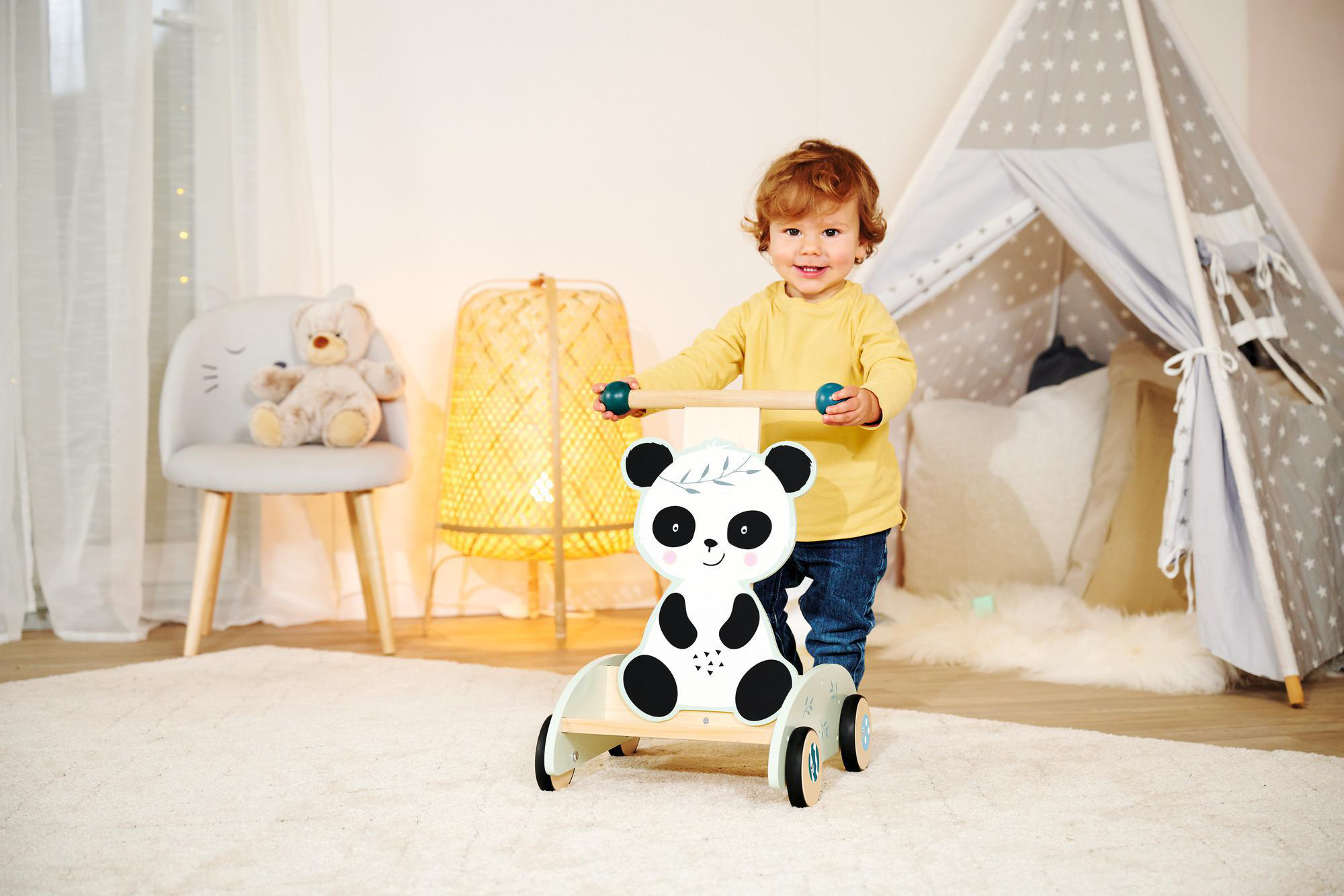 Kleinkind schiebt einen Panda-Gesicht-Walker auf einem Teppich. Zelt, Stuhl und Lampe im Hintergrund.