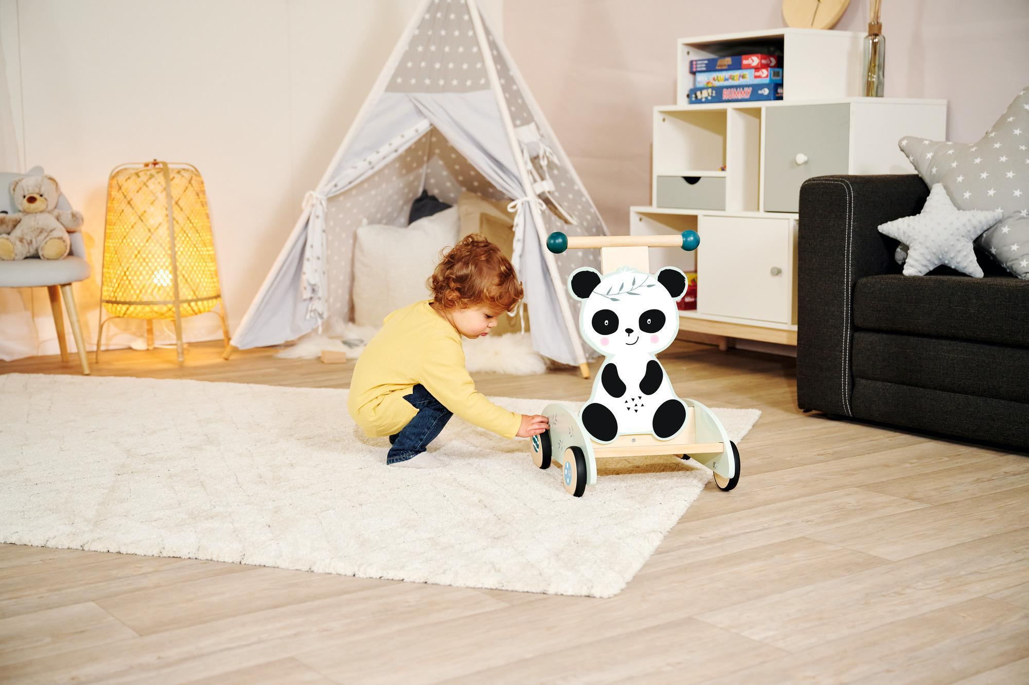 Ein Kleinkind spielt mit einem Panda-Spielzeug auf einem weißen Teppich im Kinderzimmer.