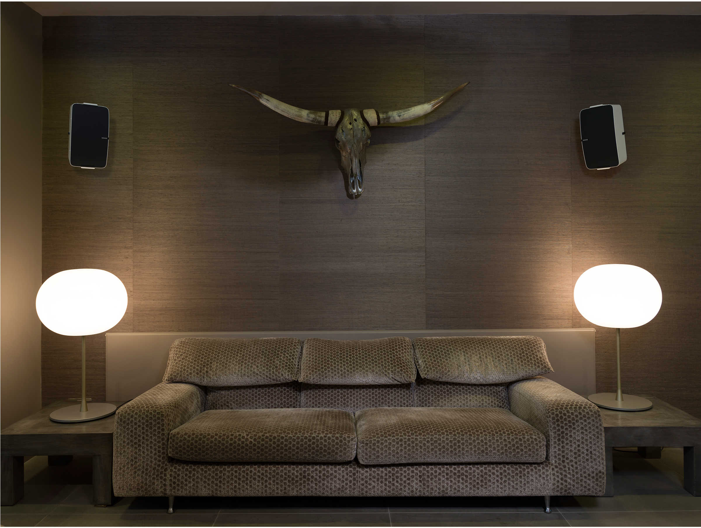 Woonkamer met twee lampen, een bank en een decoratieve schedel aan de muur.