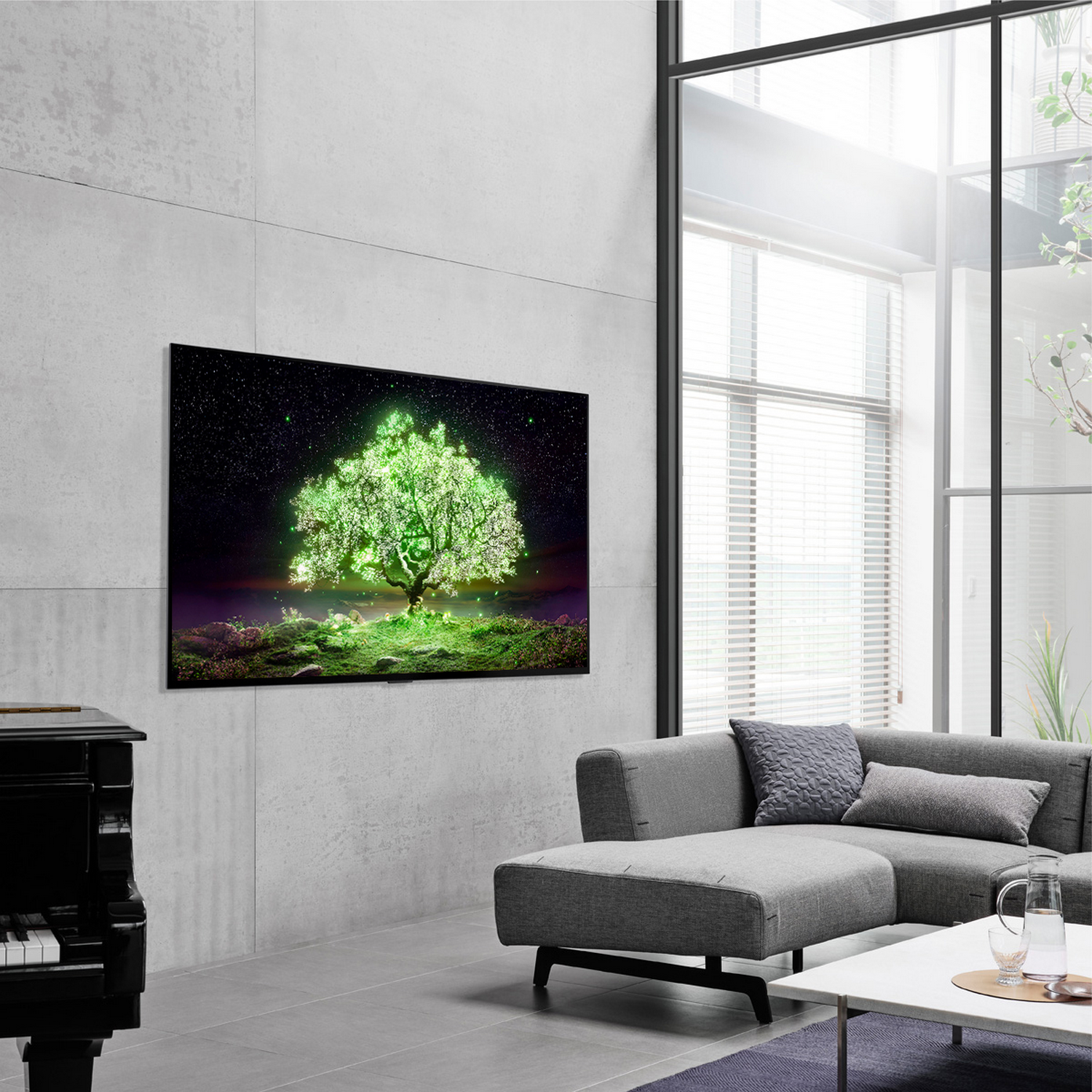 Salón con un televisor LG OLED mostrando una imagen de árbol brillante, piano y sofá gris.