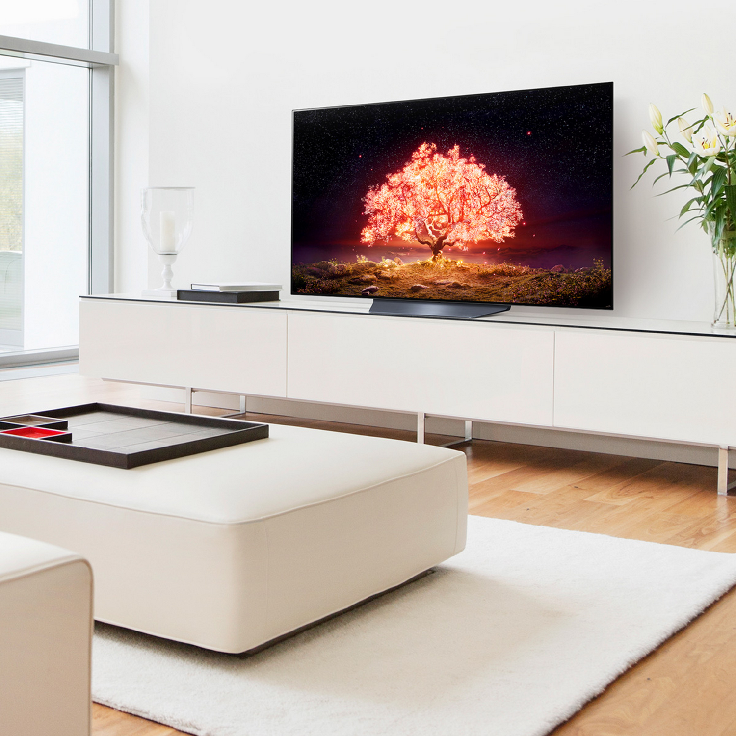 Una sala de estar con un televisor grande mostrando una imagen vibrante de un árbol, y muebles blancos.