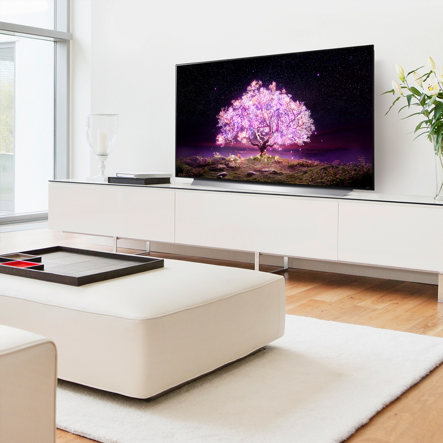 Un televisor LG OLED muestra un árbol vibrante sobre un fondo oscuro estrellado. Está en una consola blanca.