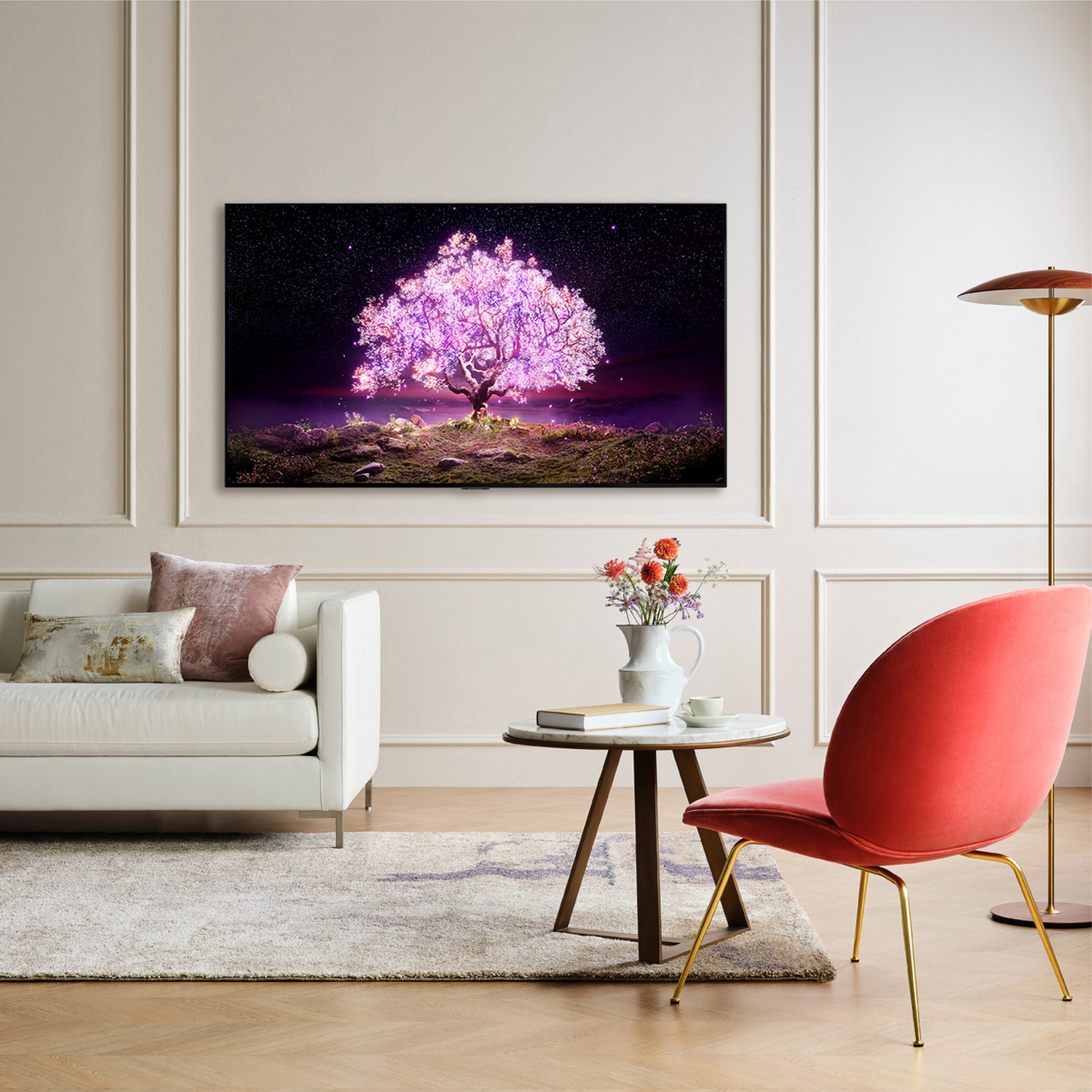 Sala de estar con TV grande mostrando imagen de árbol rosa brillante, sofá, silla y flores.