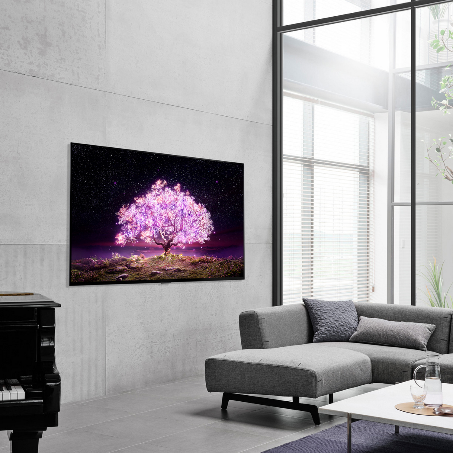 Un árbol de hojas rosas en la pantalla de un televisor en una sala de estar. Se ven un sofá, un piano y una ventana.